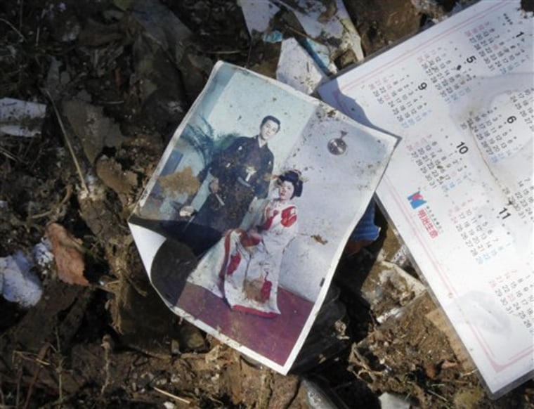 FILE - In this March 19, 2011 file photo, a wedding photo lies in the rubble in the devastated area in Onagawa in Miyagi Prefecture. The cherry trees will soon blossom in Japan. Even in normal times, the flowers are a cause for rejoicing tinged with sadness, because they fall at the moment of their greatest beauty. They are the embodiment of a notion that is central to Japanese culture - \"hakanasa,\" a hard-to-translate word that conveys the fragility, or evanescence, of life. In this time of national grieving, the cherry blossoms will bring home the awareness of hakanasa with a strange kind of force, one that doesn't strike but sinks into the soul like heat from a hot spring or fire from a sake bottle, bringing sorrow and solace in equal measure. (AP Photo/Shuji Kajiyama, File)